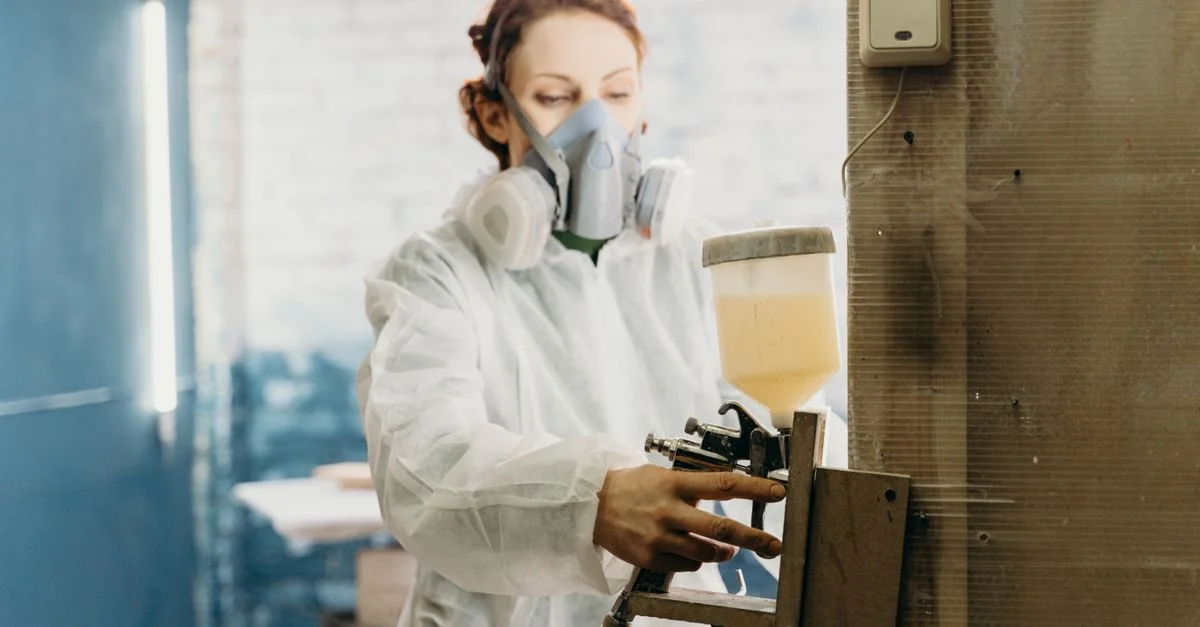 Femme portant un équipement de protection utilisant un pistolet à peinture dans un atelier industriel.