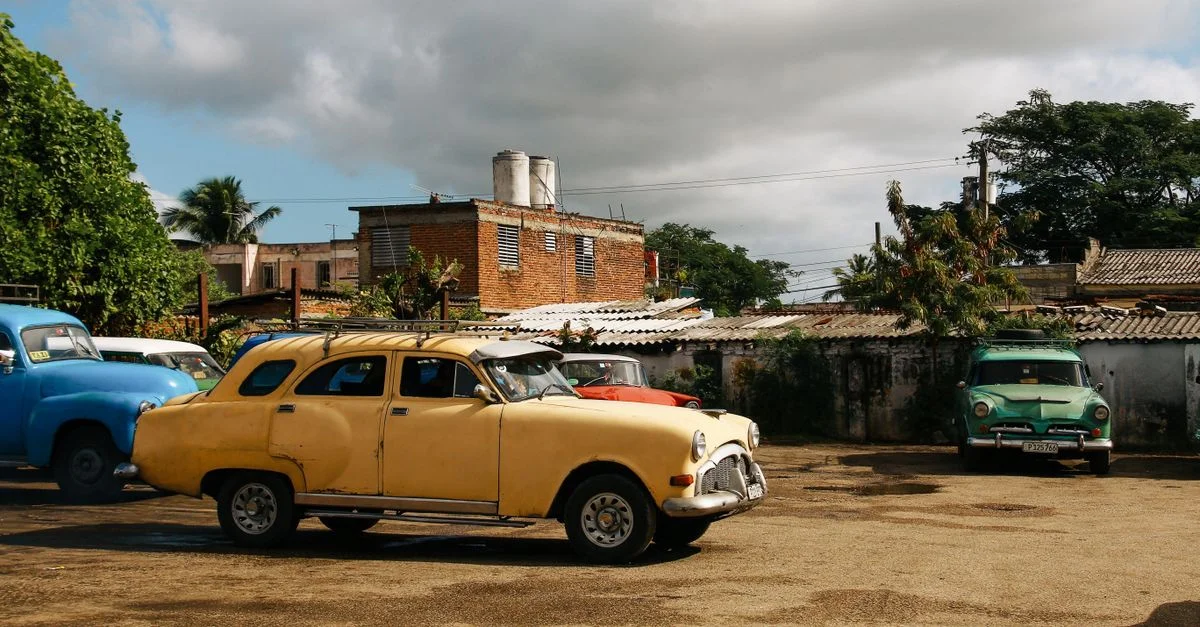 Une collection de voitures classiques anciennes dans un parking sous un ciel nuageux.