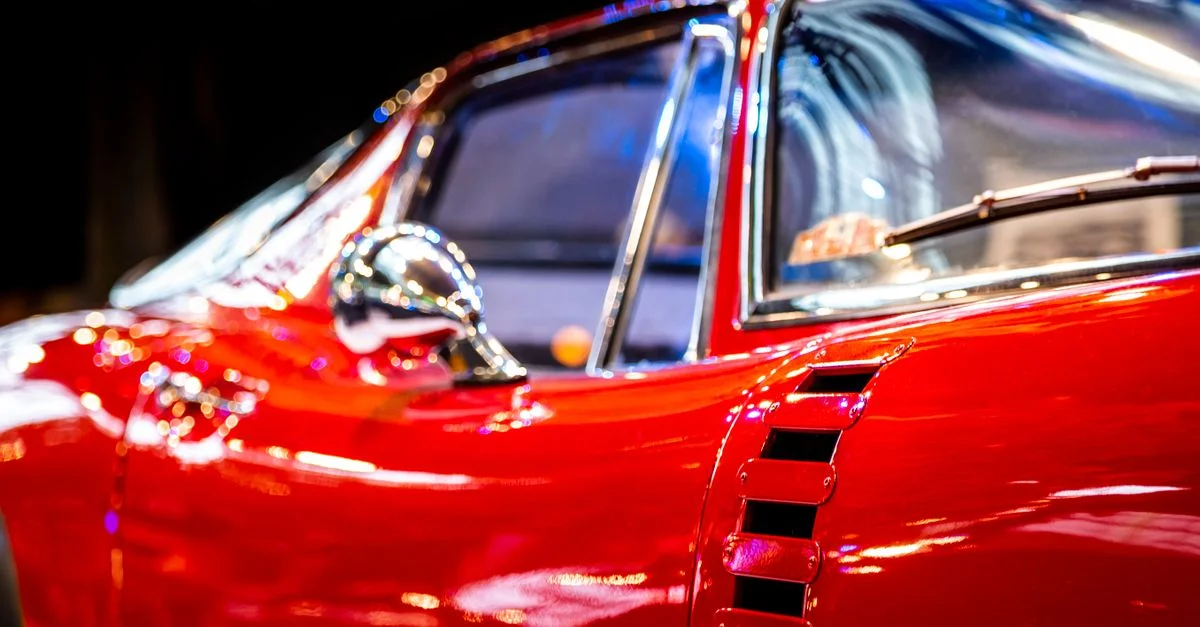 Vue latérale d'une voiture ancienne rouge brillante sous les lumières de la ville, mettant en valeur ses détails chromés.