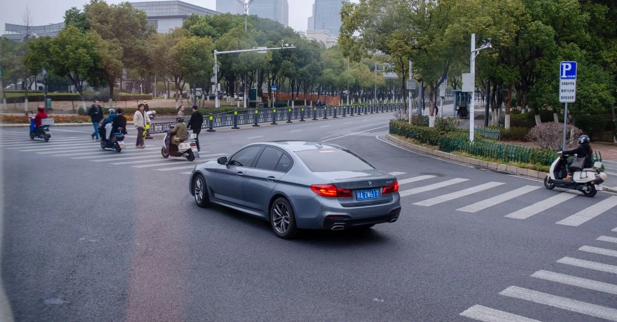 Intersection de rue animée avec des voitures, des scooters et des piétons par une journée nuageuse.