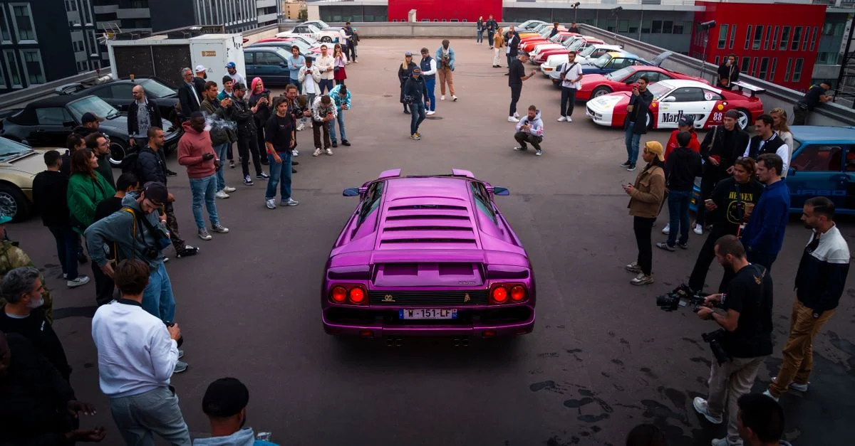 Des passionnés se rassemblent autour d'une voiture de sport violette vibrante sur un parking sur le toit.
