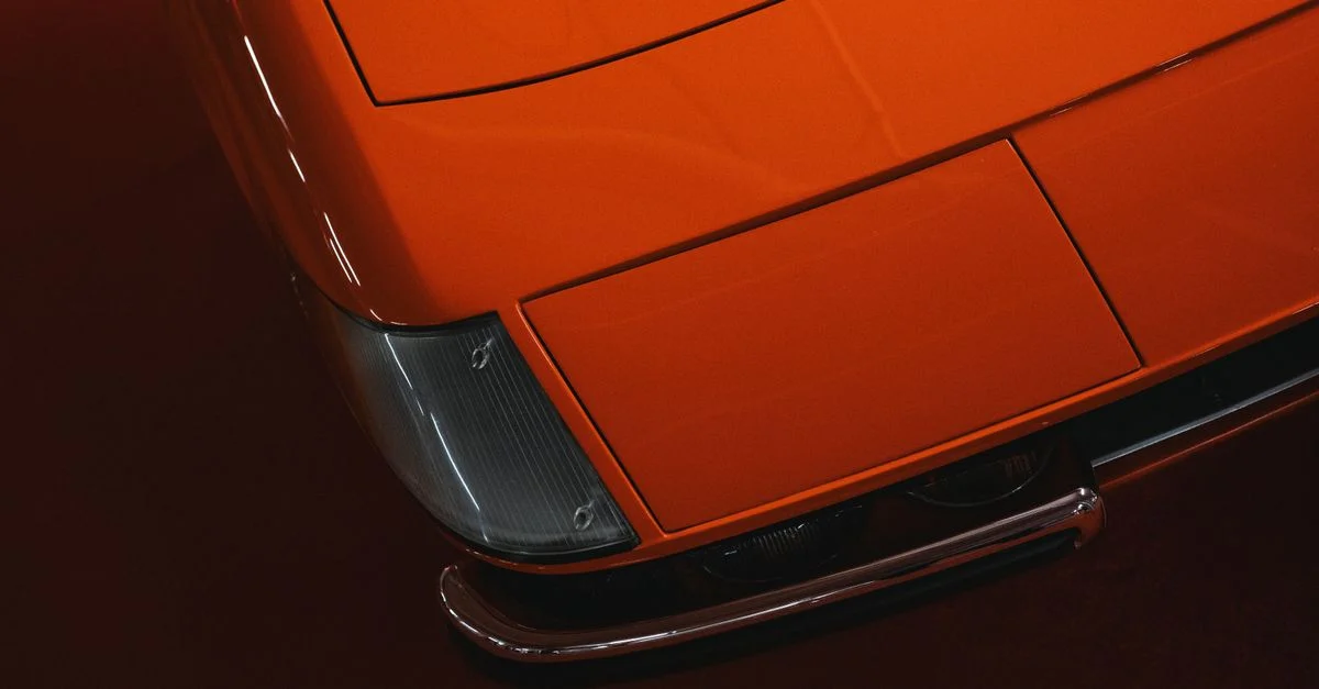 Vue détaillée du capot d'une voiture de sport orange avec des détails chromés, soulignant l'esthétique luxueuse et vintage.