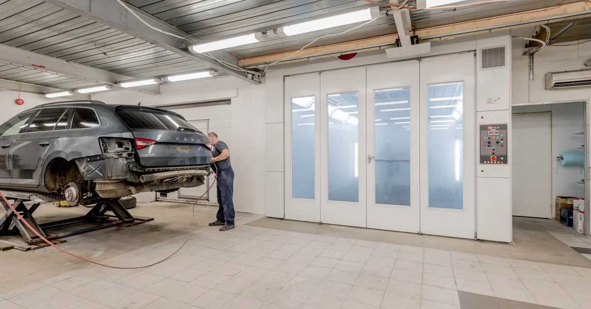 Mécanicien réparant une voiture à l'intérieur d'un atelier automobile, se concentrant sur l'entretien du véhicule.