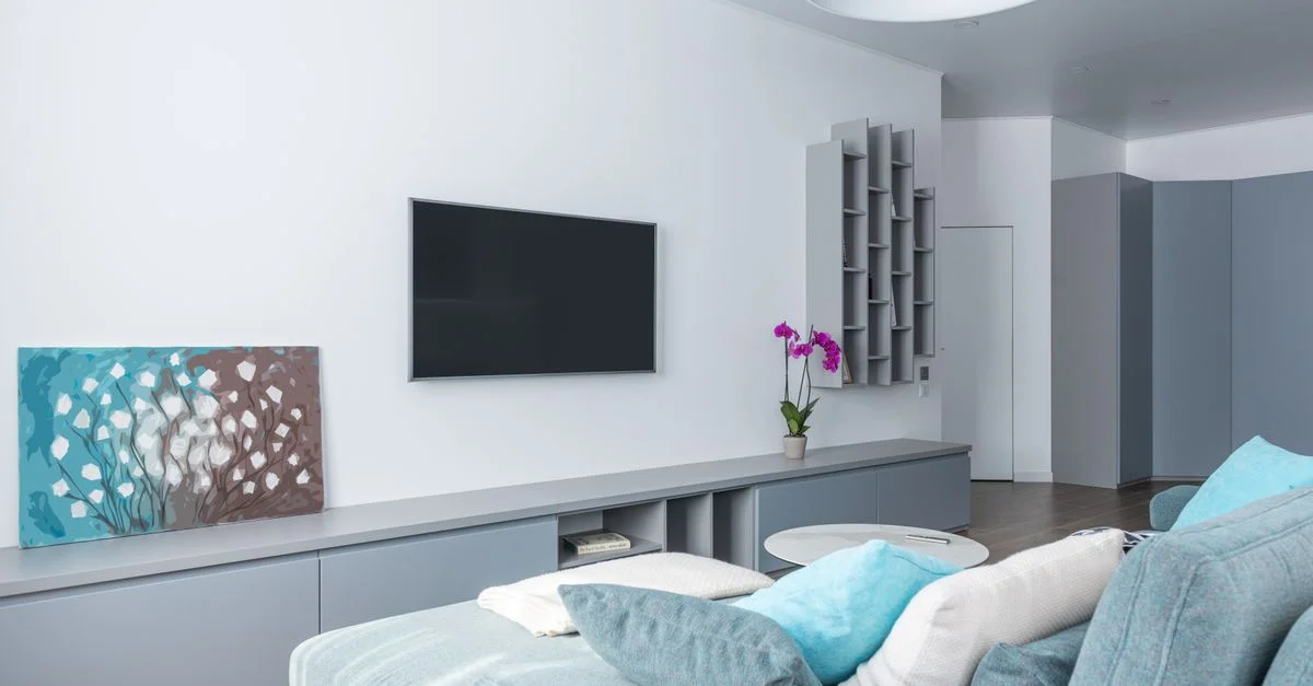 Salon contemporain au design minimaliste, avec un canapé bleu et une télévision murale.
